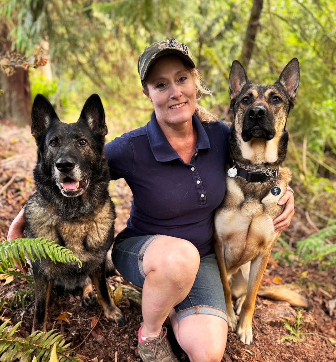 Belynda Moore, professional dog trainer, kneeling outdoors with two well-trained German Shepherds at Ultimate K9