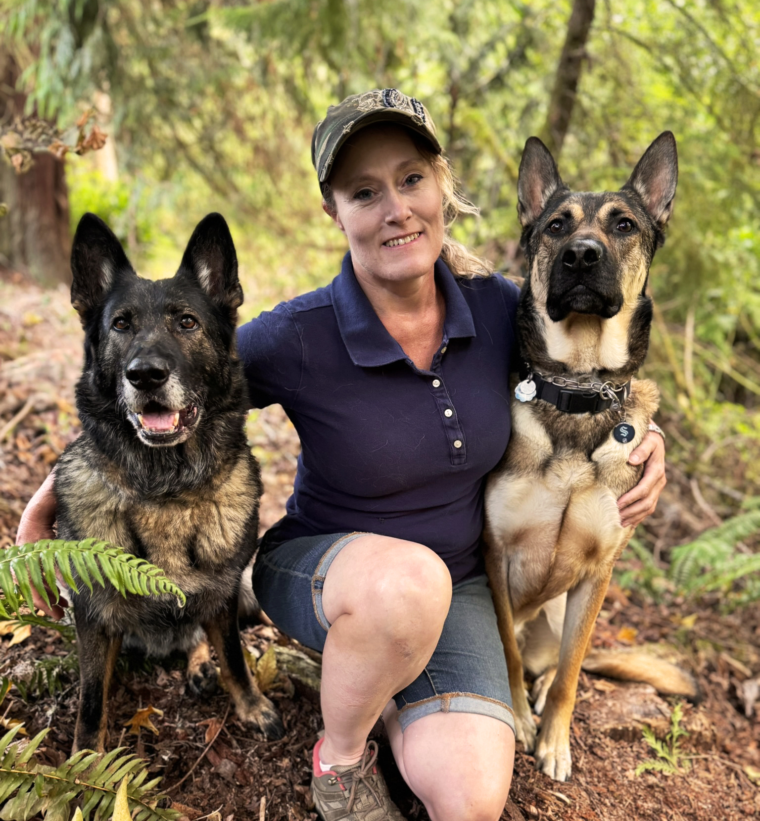 Belynda Moore, professional dog trainer, kneeling outdoors with two well-trained German Shepherds at Ultimate K9